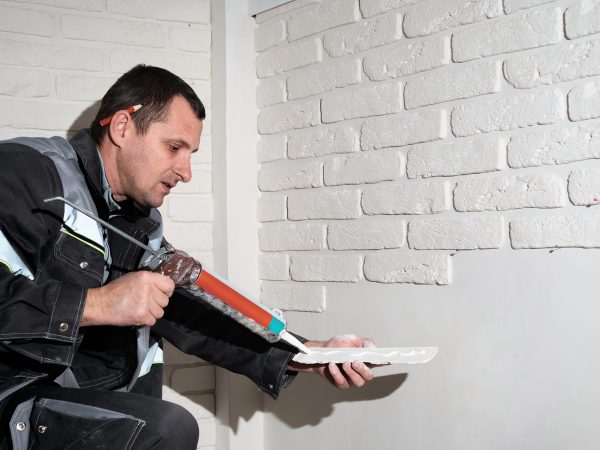 Master applies glue tiles for facing the house. The master builder decorates the walls of the apartment. Finishing the building with modern materials.